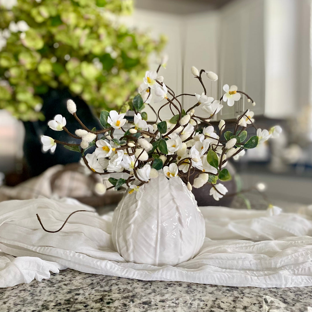 A set of three artificial white floral picks with green leaves, arranged in a white ceramic vase on a granite countertop.