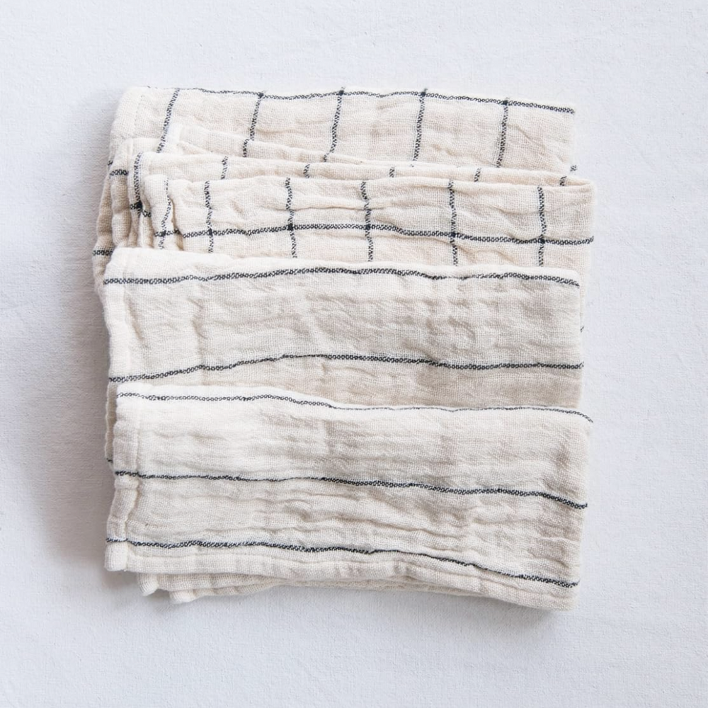 A set of four folded striped cotton napkins in beige and black colors with a plaid pattern on a white background.