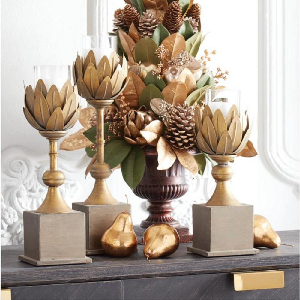 Decorative arrangement with gold artichoke sculptures, a vase with flowers, and gold pears on a table.