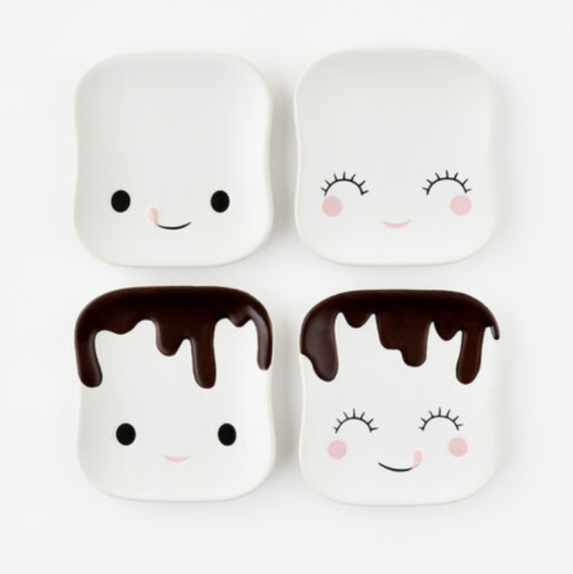 A set of four ceramic dessert plates, each with a different marshmallow character design. Two have smiling faces and two have a chocolate-dipped marshmallow appearance.