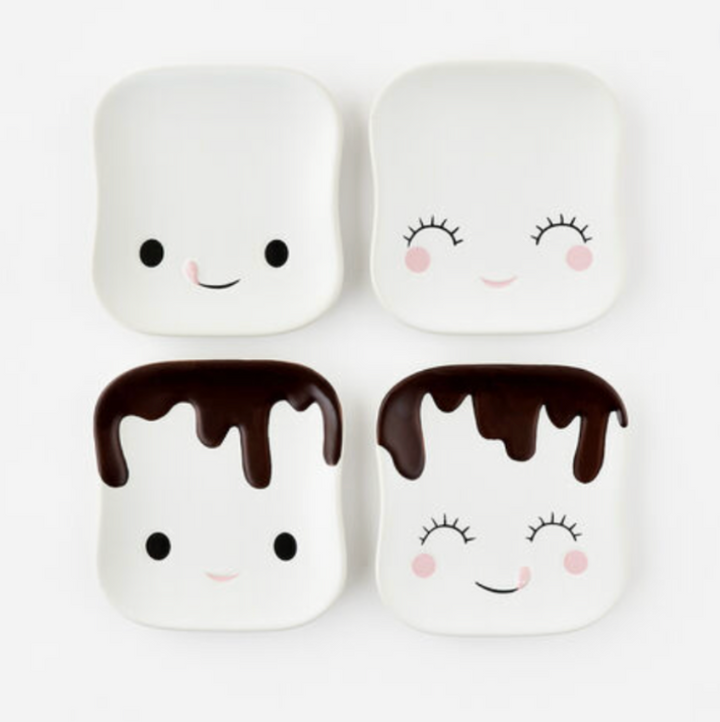 A set of four ceramic dessert plates, each with a different marshmallow character design. Two have smiling faces and two have a chocolate-dipped marshmallow appearance.