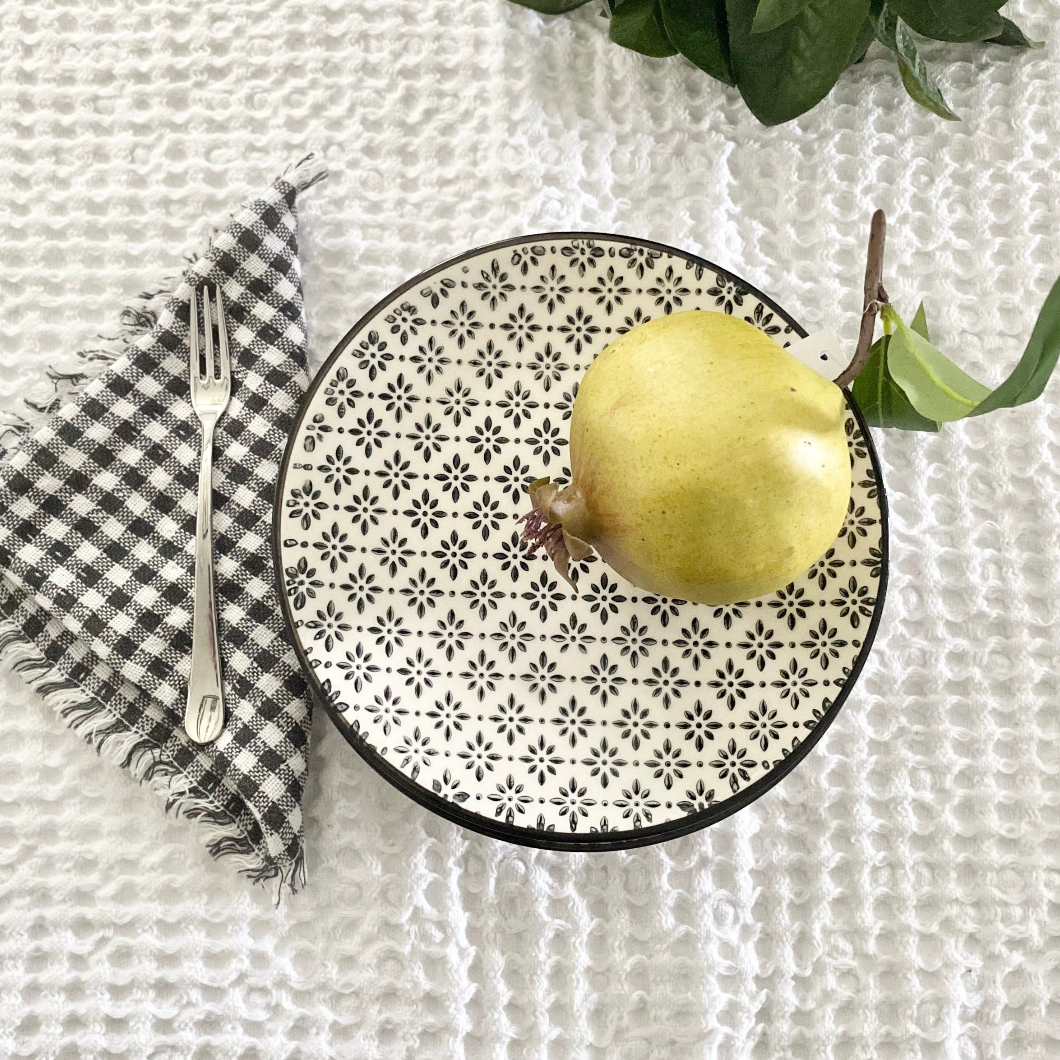 Decorative plate with a pear on a textured white surface with a checkered napkin and fork.
