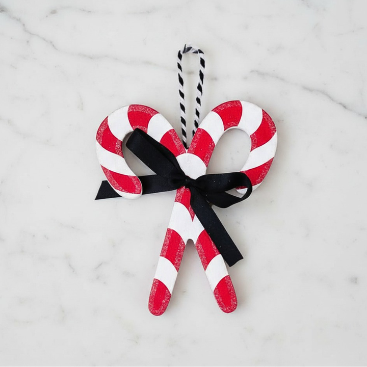 Decorative candy cane ornament with a black ribbon on a marble surface