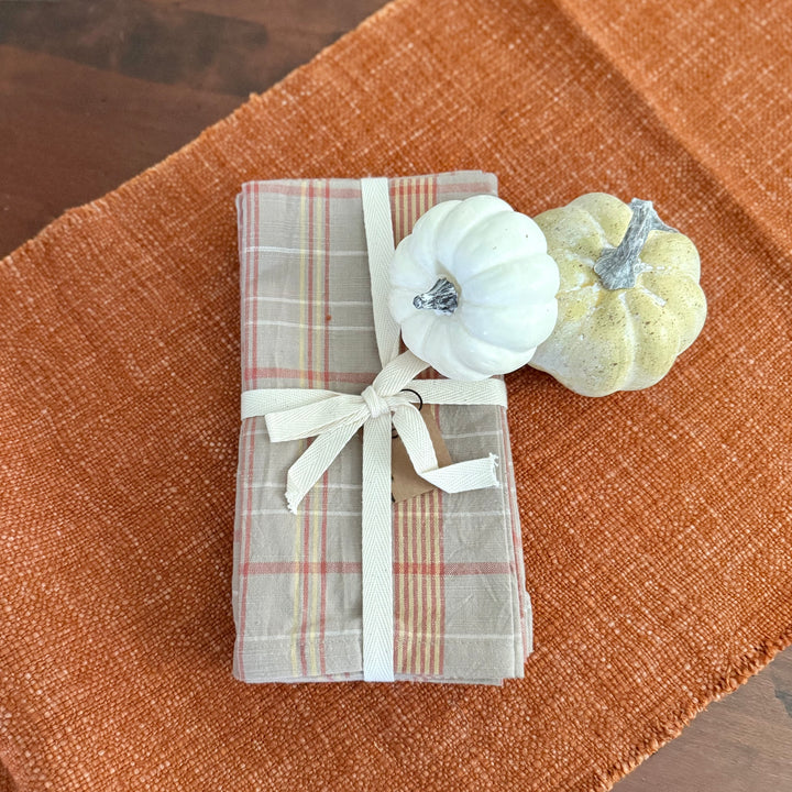 Folded plaid fabric with a white ribbon on a brown textured surface with small pumpkins.