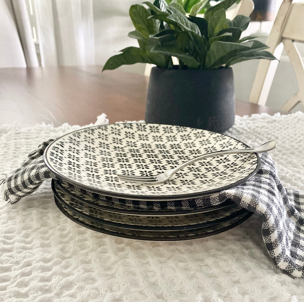 Stack of black and white patterned plates on a textured surface with a plant in the background.