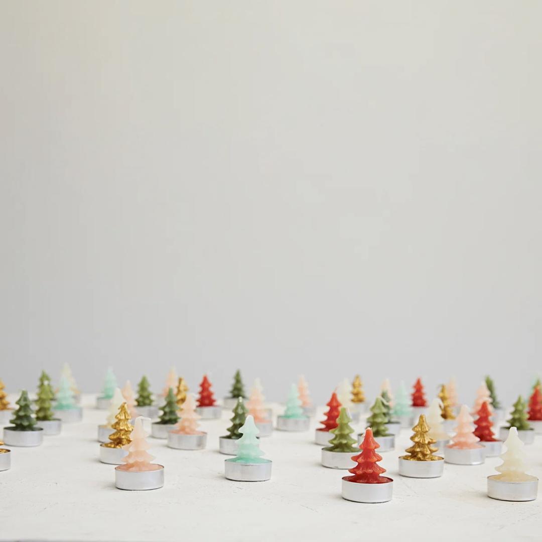Small Christmas tree candles in various colors on a white surface with a light gray background