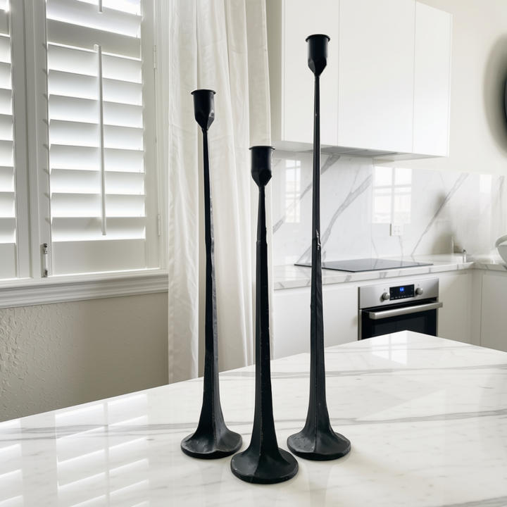 Three black iron candlesticks of varying heights arranged on a white marble kitchen island in a modern kitchen setting.