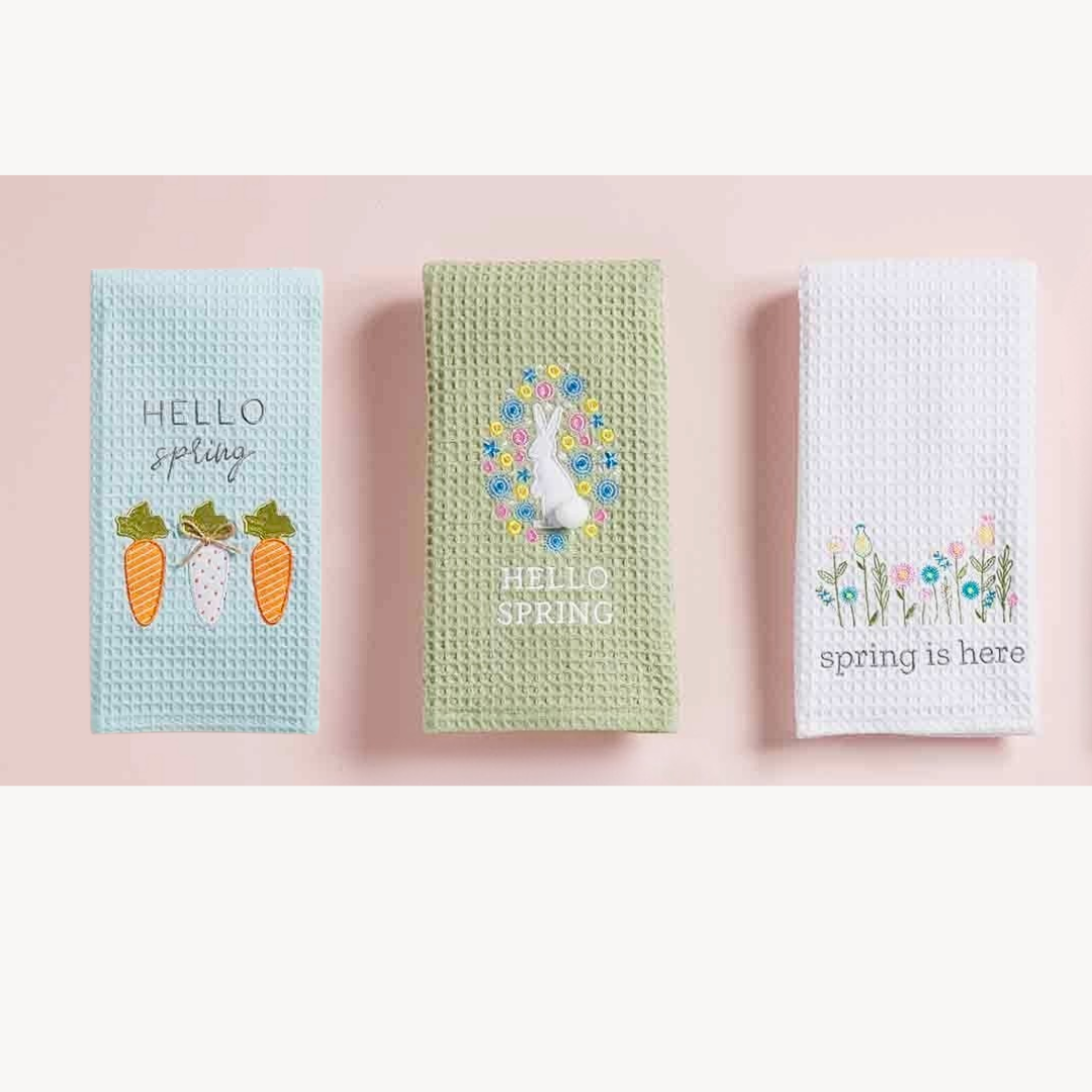 Three spring-themed waffle weave hand towels with decorative elements on a pink background