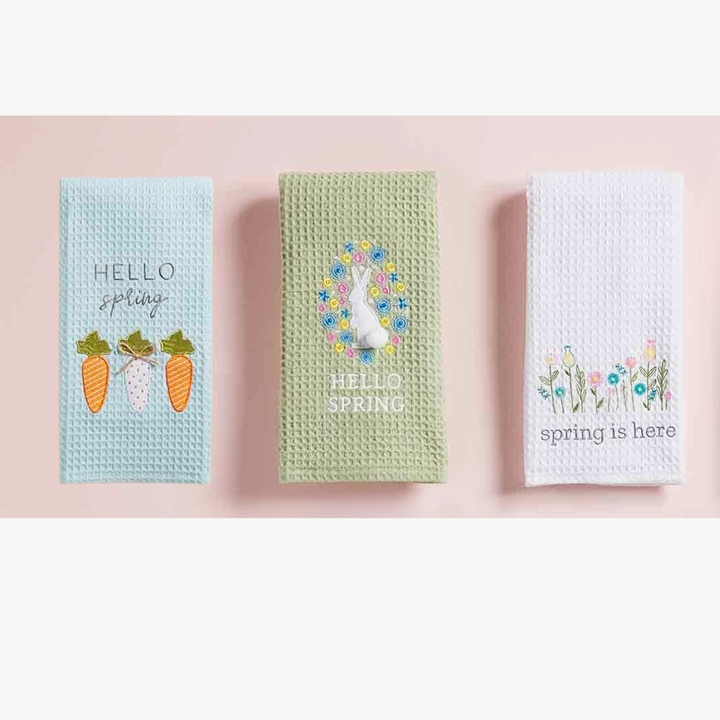 Three spring-themed waffle weave hand towels with decorative elements on a pink background