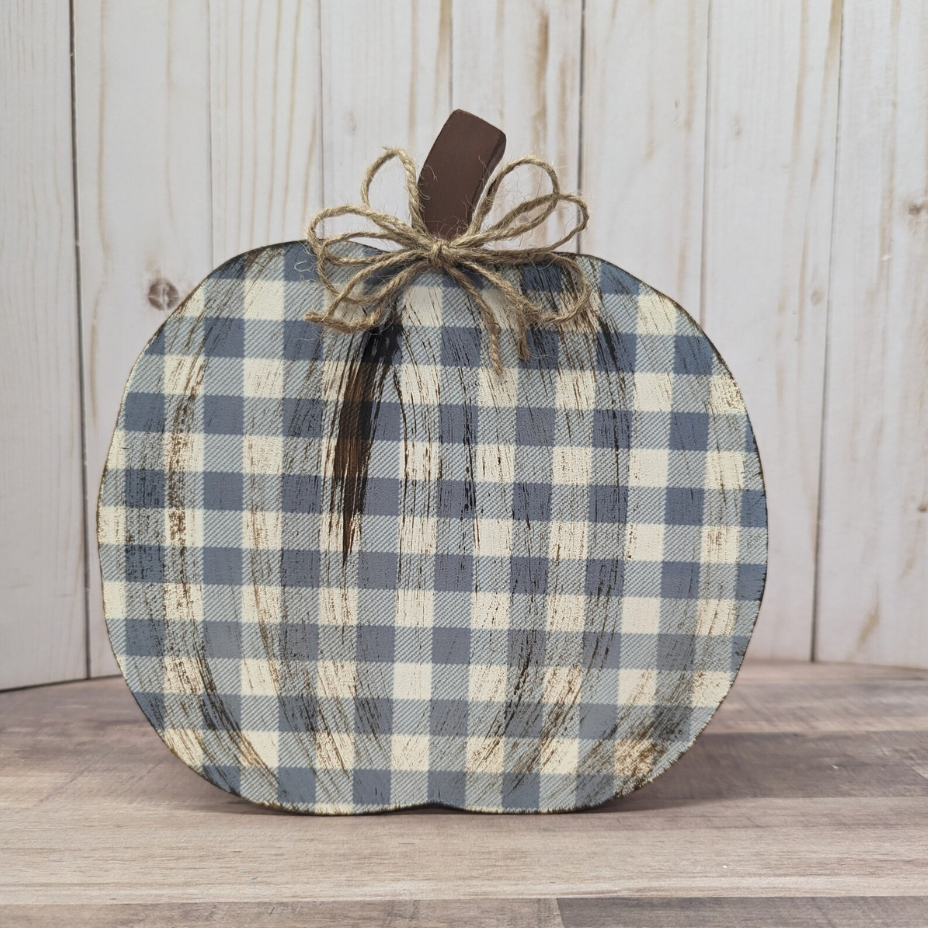 A rustic decorative pumpkin with a blue and beige gingham pattern, featuring a dark brown faux-wood stem and a jute twine bow, set against a light wood plank background.