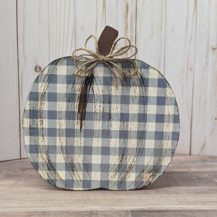 A rustic decorative pumpkin with a blue and beige gingham pattern, featuring a dark brown faux-wood stem and a jute twine bow, set against a light wood plank background.