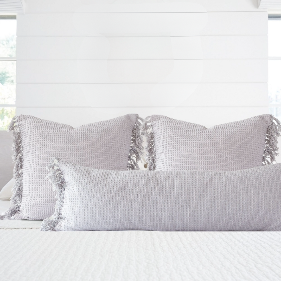 Gray textured pillows with tassels on a white bed