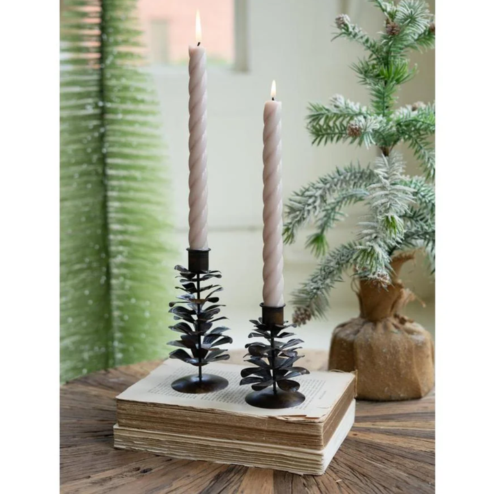 Decorative candle holders with candles on a wooden block, surrounded by greenery.