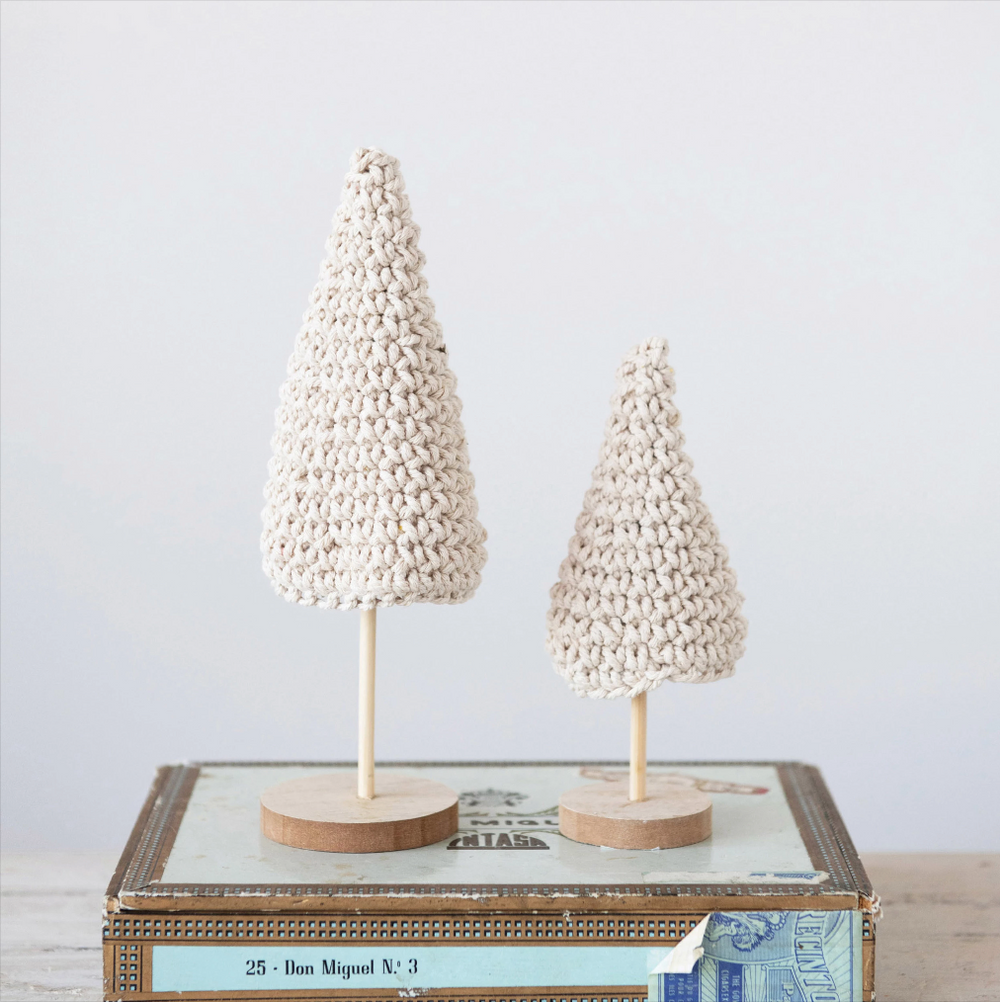 Two crocheted Christmas trees with a vintage cream-colored design, standing on wooden bases, placed on a decorative box.