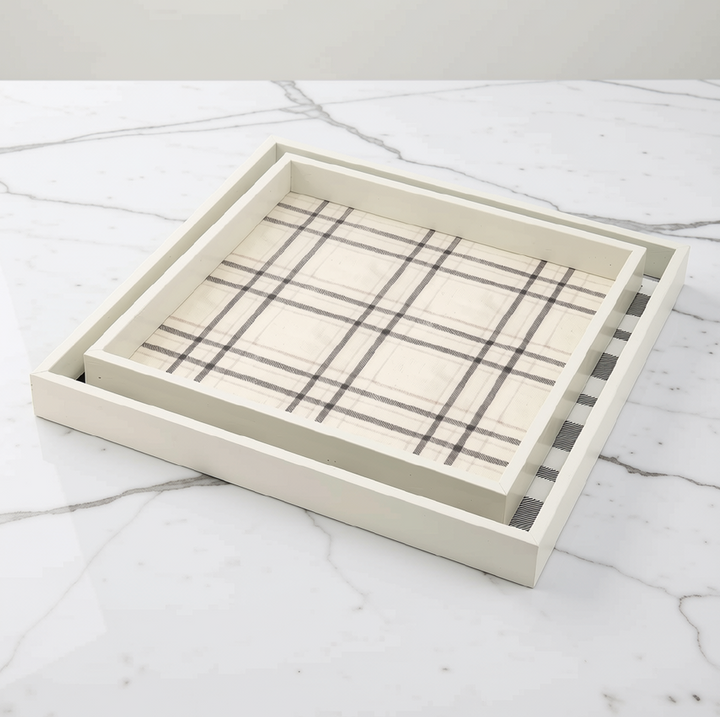 A square nesting tray set with a cream-colored wooden frame and a plaid patterned insert, displayed on a white marble surface.