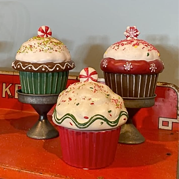 Decorative Christmas-themed cupcake figurines on a red surface with a light blue background.