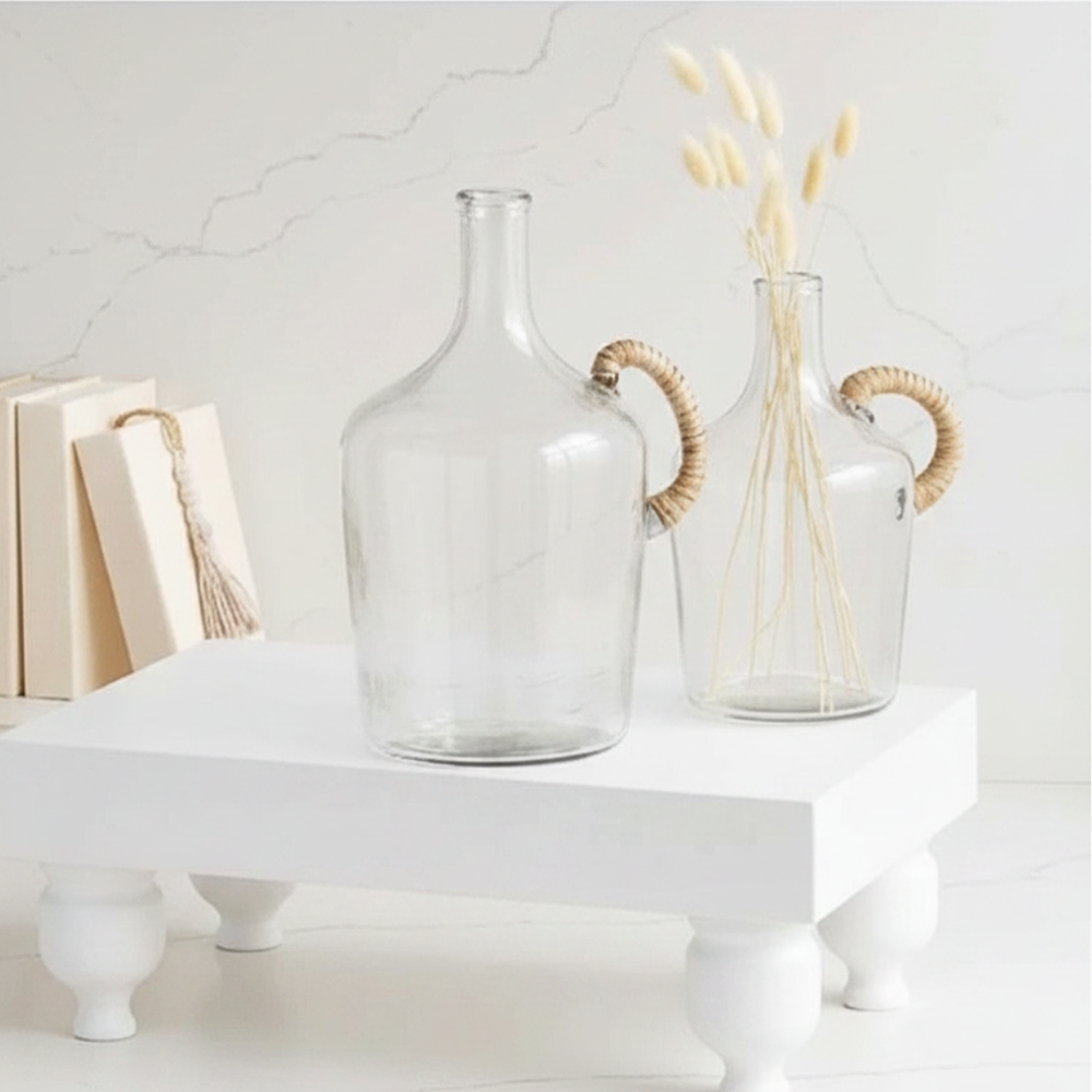 Two clear glass vases with woven handles on a white surface.