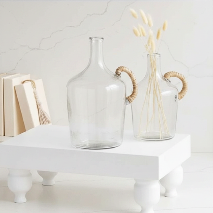 Two clear glass vases with woven handles on a white surface.