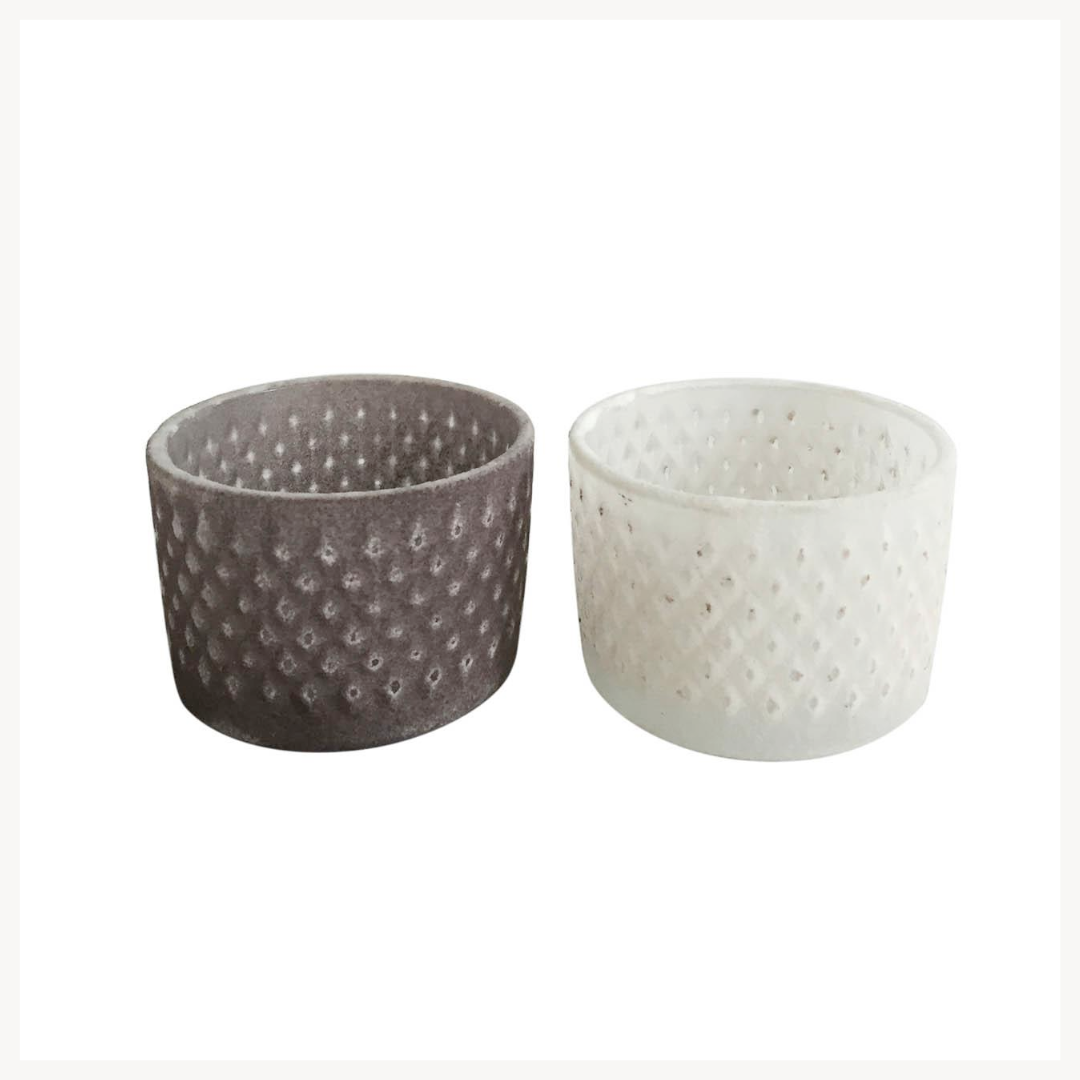 Two textured votive candle holders, one gray and one white, on a white background.
