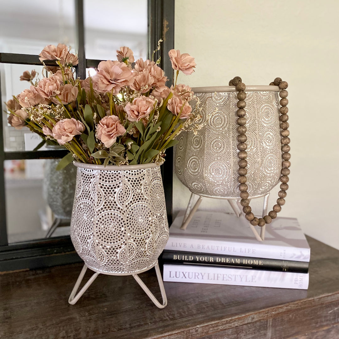 Two iron containers with whitewash finish and scroll design textures, one large and one small, on a tabletop displaying flowers.