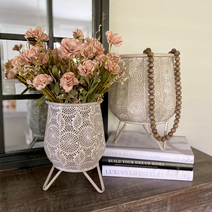 Two iron containers with whitewash finish and scroll design textures, one large and one small, on a tabletop displaying flowers.