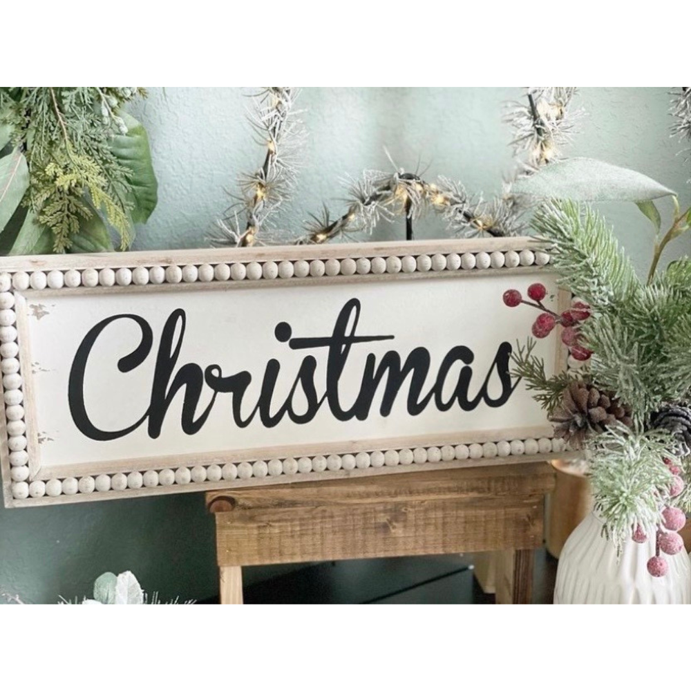 Decorative sign with 'Christmas' text on a festive background with greenery and lights.