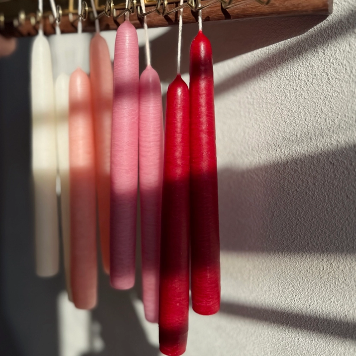 Set of red and pink taper candles hanging on a hook against a neutral background