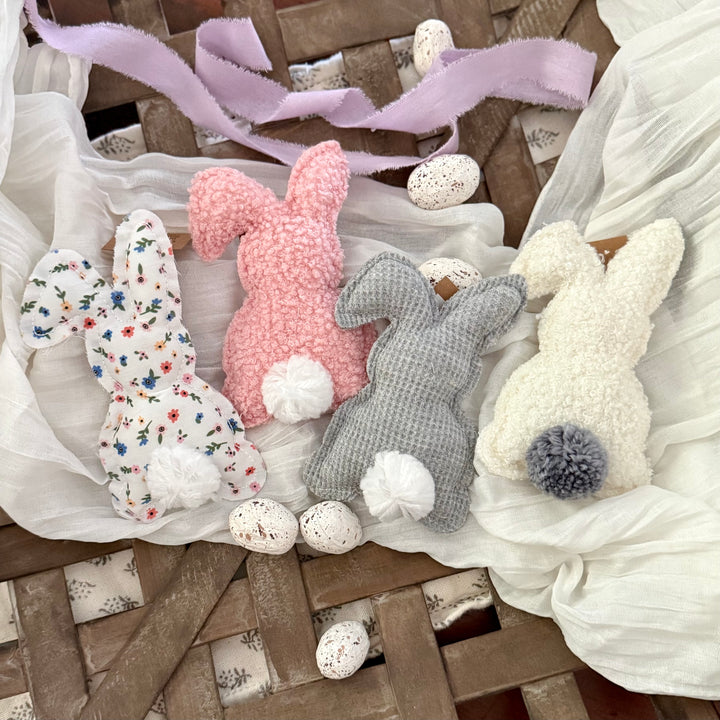 Four fabric Easter bunnies in different colors on a wooden surface with decorative eggs and ribbons.