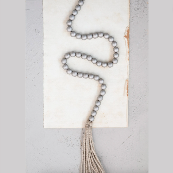 A silver bead garland with jute tassels, laid out on a white surface.