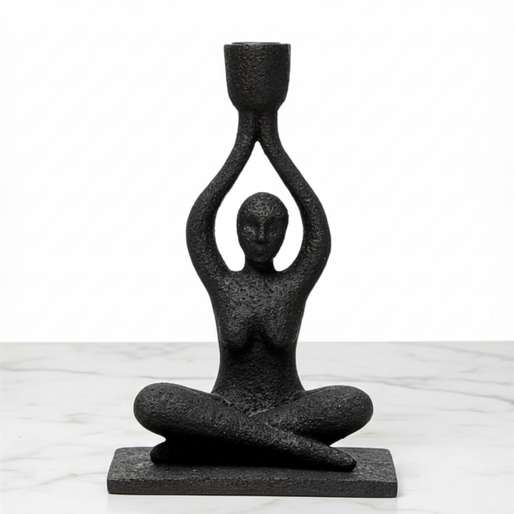 Black resin sculpture of a seated figure holding a bowl on a white background
