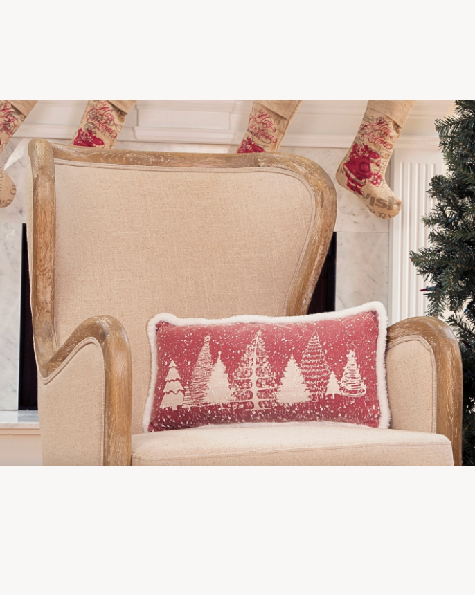 Decorative pillow with Christmas tree pattern on a beige armchair in front of a fireplace.