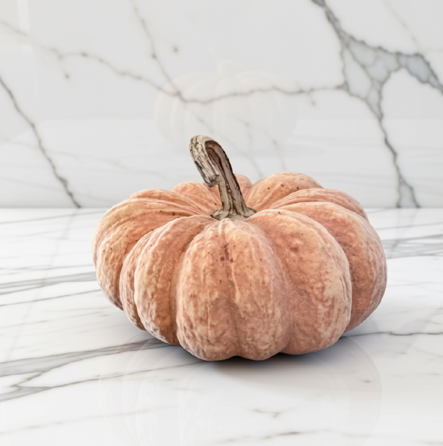 A decorative orange pumpkin with a textured, ribbed surface and a short brown stem, placed on a white marble surface with a matching marble background.