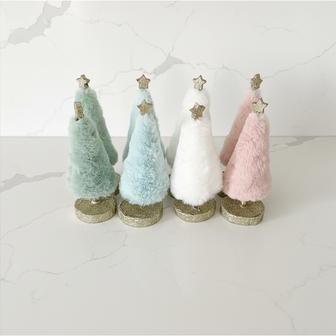 Four small decorative Christmas trees in green, blue, white, and pink with glittery bases on a light background.