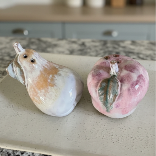 Two stoneware salt and pepper shakers apple and pear shaped on a kitchen counter.