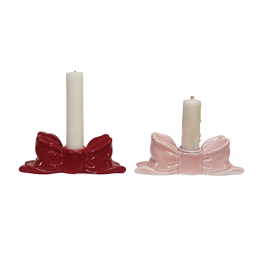 Two stoneware candle holders with bows, one red and one pink, on a white background.