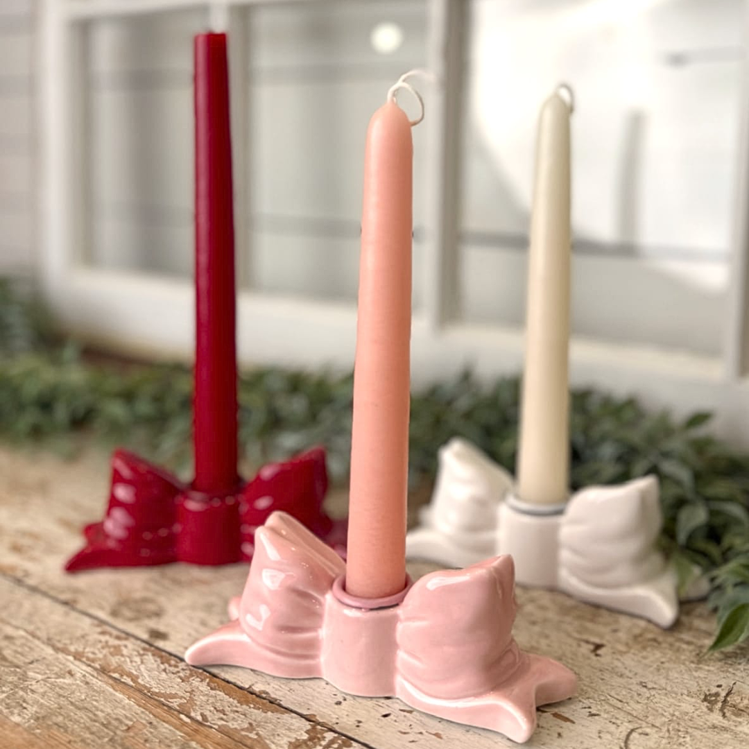 Set of three candles in red, pink, and beige in decorative holders on a wooden surface with a blurred indoor background.