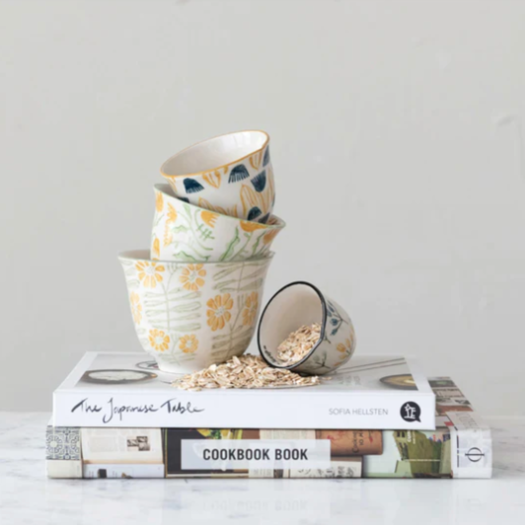 Stack of ceramic bowls with floral patterns on top of cookbooks.