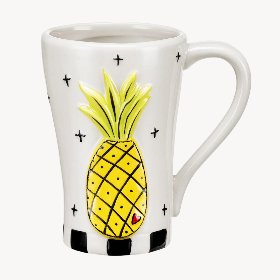 A ceramic mug with a white background featuring a yellow pineapple with black 'x's' and an embossed heart accent.