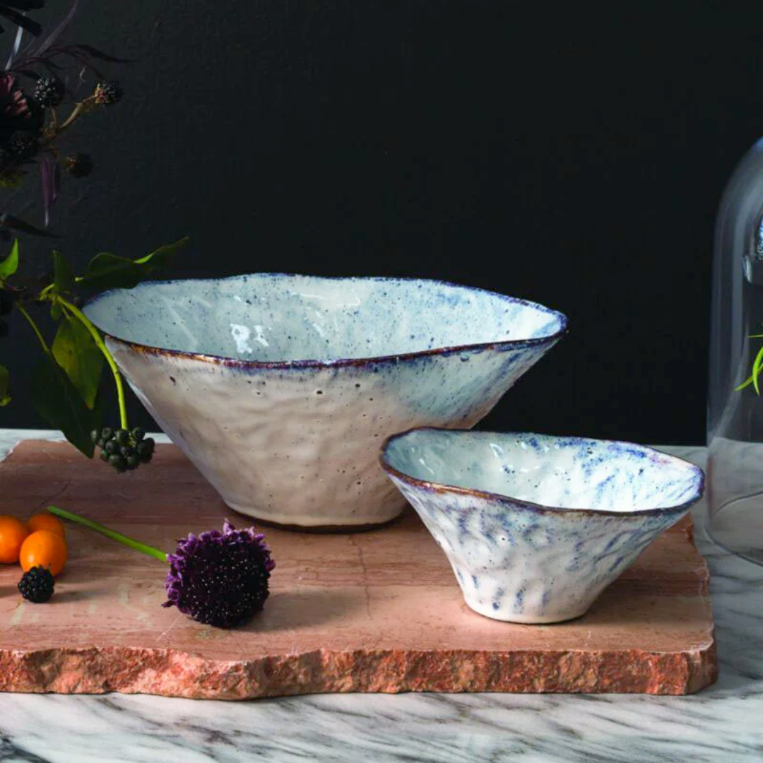 Two ceramic bowls with a speckled design on a wooden board with a dark background.