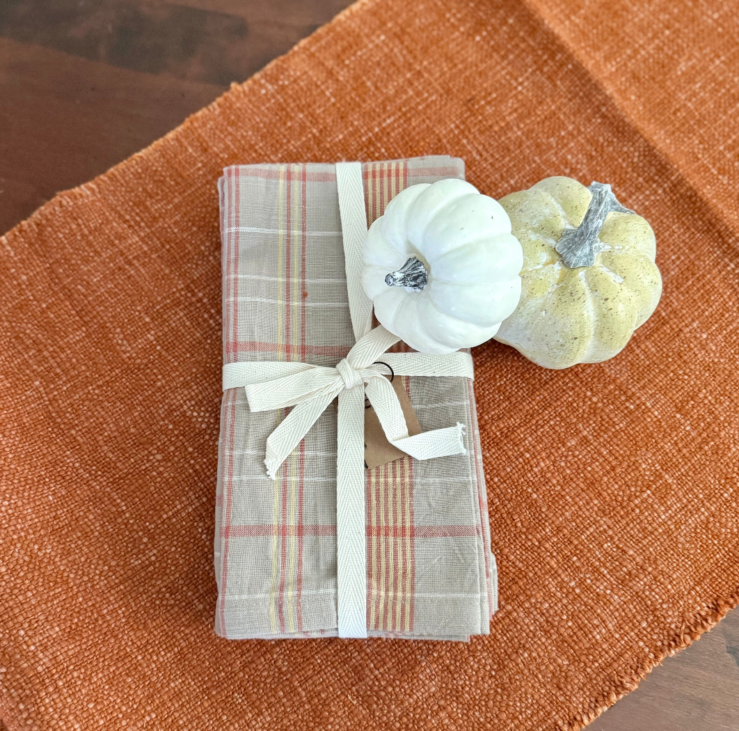 Plaid napkin with a white bow and two small pumpkins on a terracotta table runner