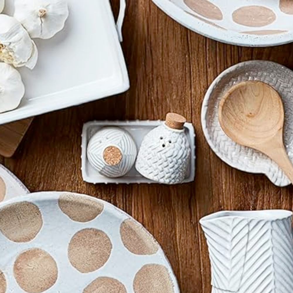 Ceramic salt & pepper set and a wooden spoon on a wooden surface.