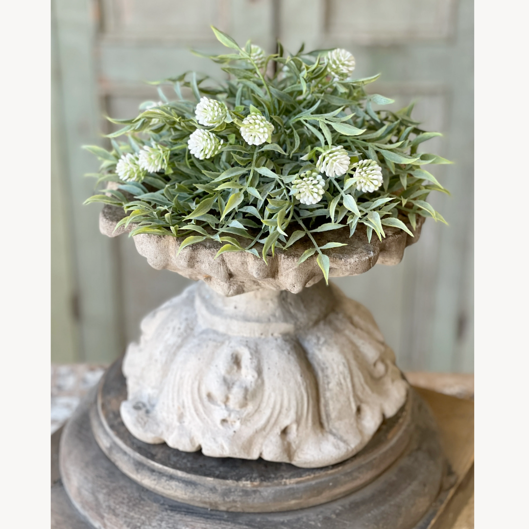 Decorative stone pedestal with a topiary of greenery and white flowers.