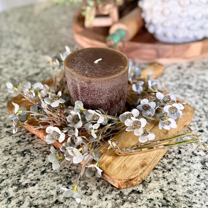 Candle in a candle ring with blue flowers on a wooden cutting board on a granite surface