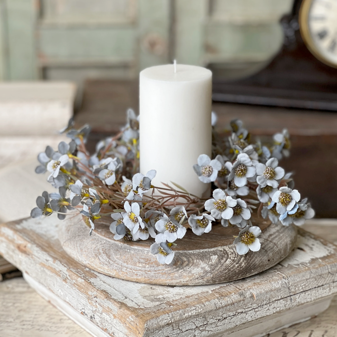 Decorative candle ring with blue flowers and a candle on a wooden surface.