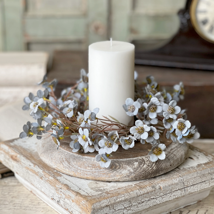Decorative candle ring with blue flowers and a candle on a wooden surface.
