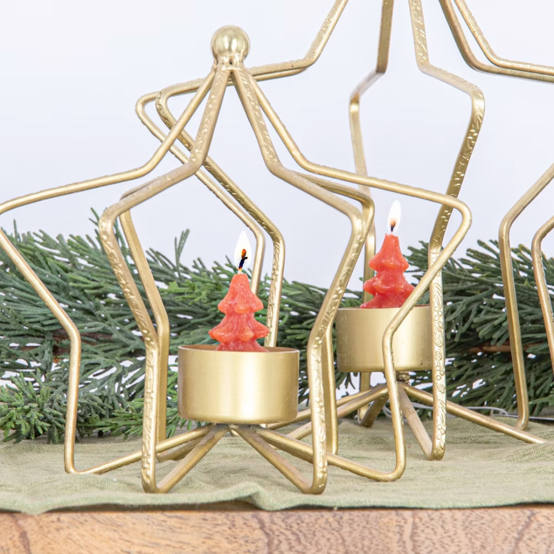 Gold candle holders with red candles on a surface with greenery in the background