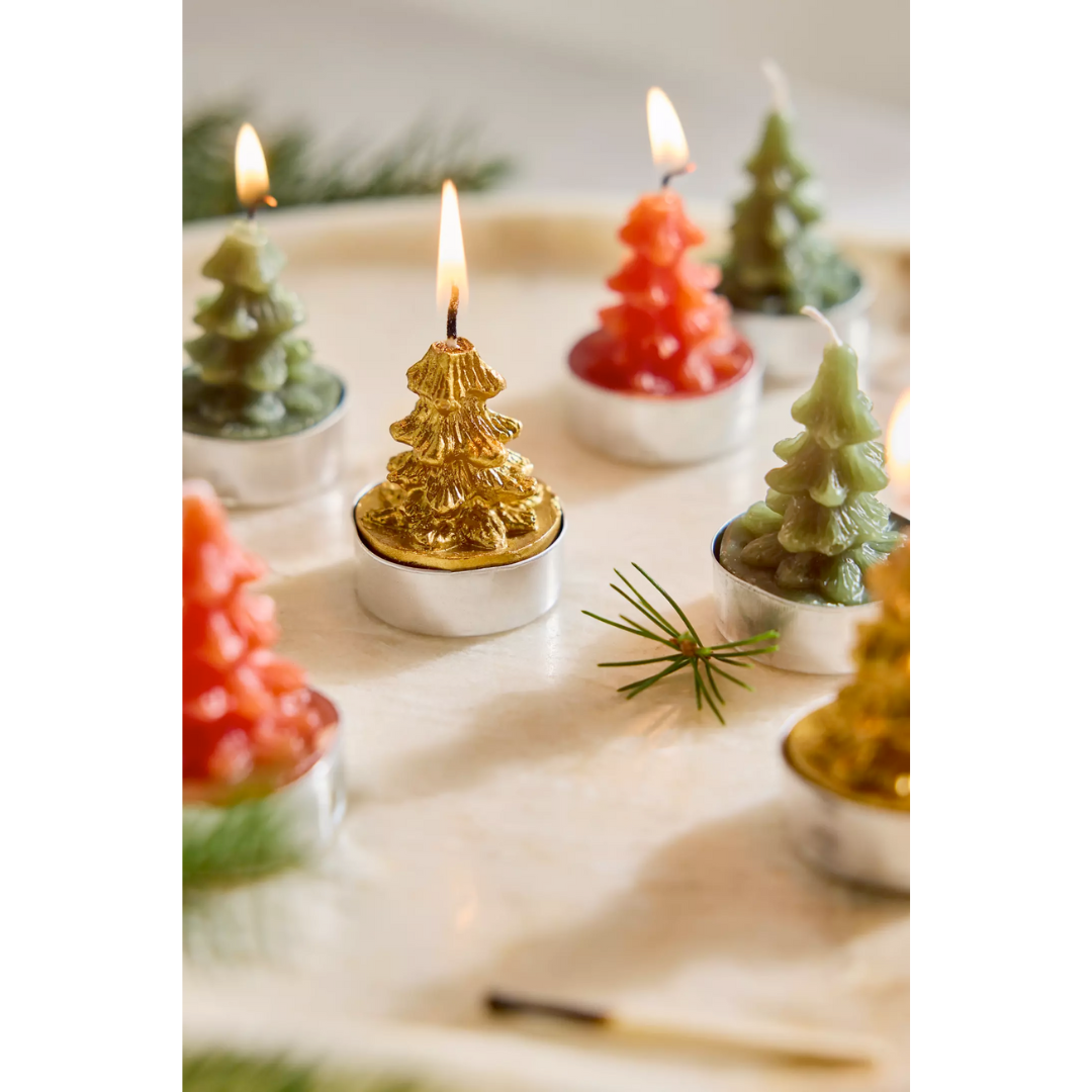 Decorative candles shaped like Christmas trees on a white surface with greenery.