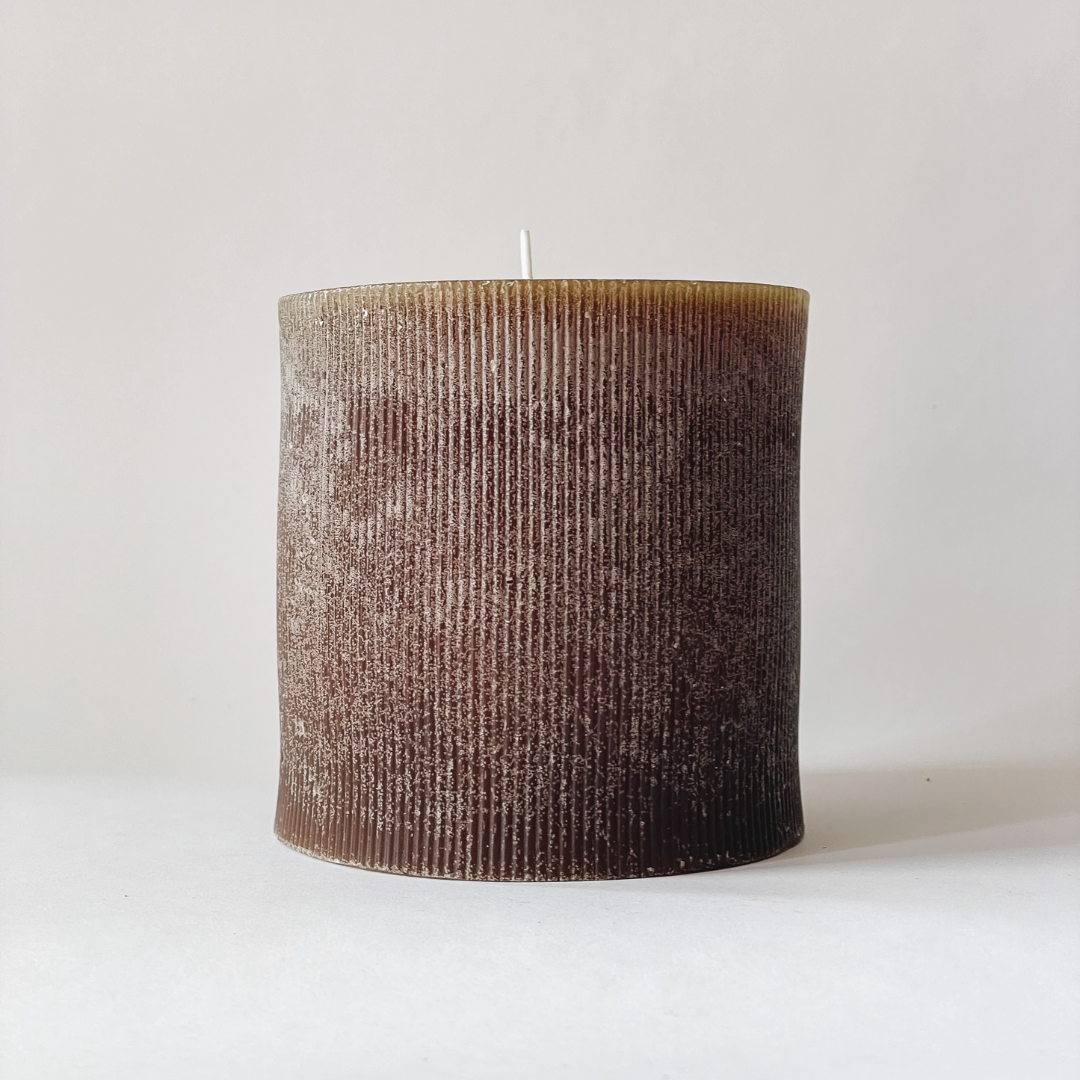 A pleated pillar candle in a brown color with a rustic texture, displayed against a neutral background