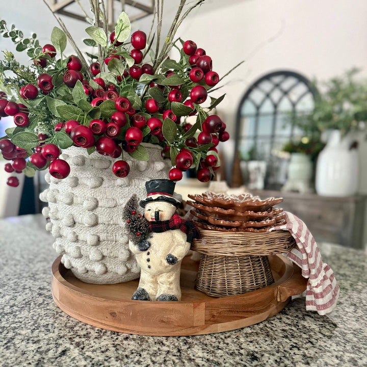 Decorative holiday setting with a vintage snowman, striped towel, snowflake plates, red pod berries in a knotted vase
