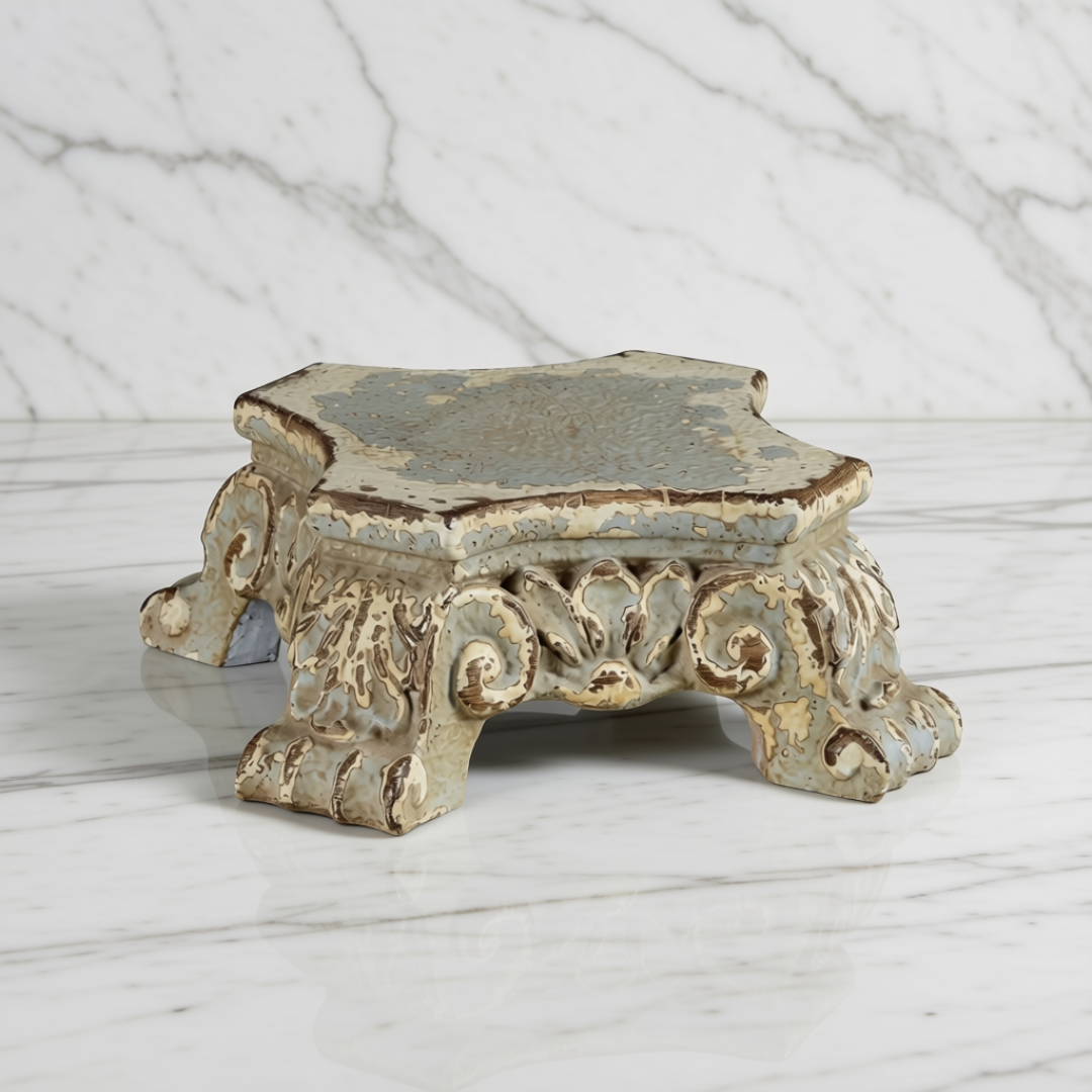 An ornate vintage-style resin pedestal riser with a distressed blue-gray and beige glaze, set against a white marble background.